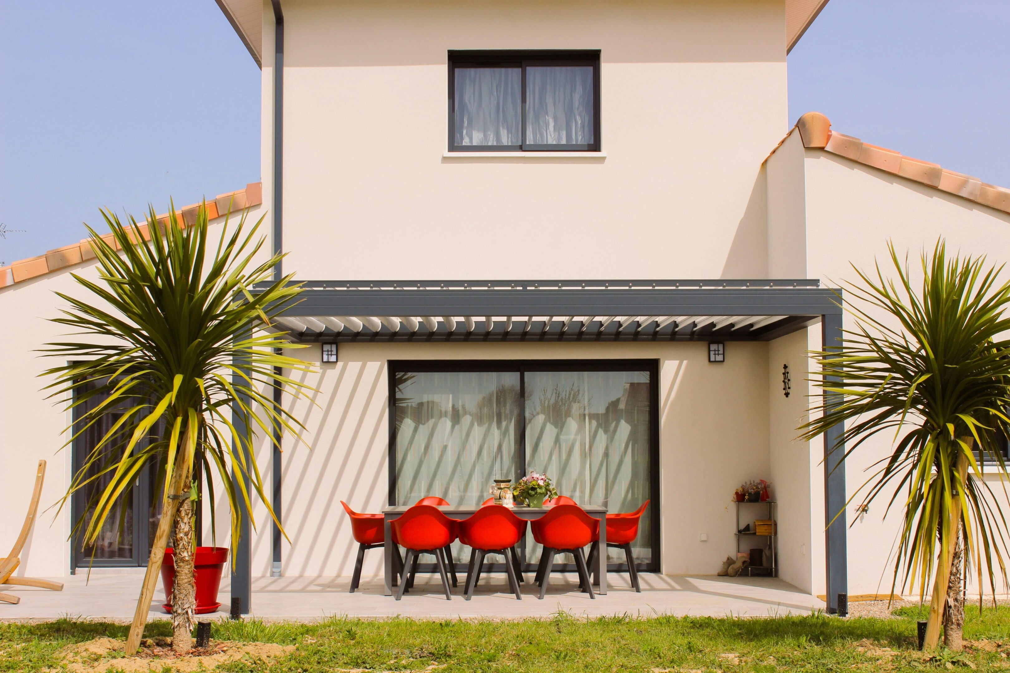 A patio with red chairs and a table outside of it